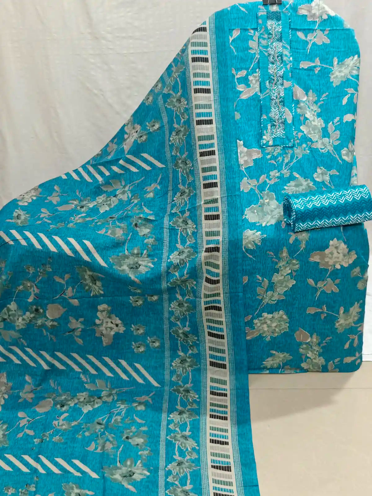 Turquoise blue printed cotton fabric set with a floral pattern and a striped border, shown draped on a white background.