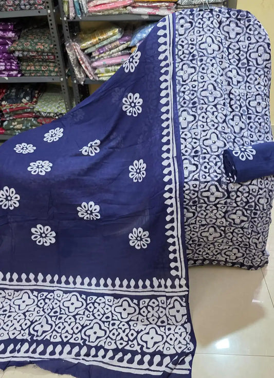 Classic black unstitched cotton salwar kameez material displaying a detailed white interlocking geometric batik pattern with small mirror accents across the main shirt fabric, styled with a rolled black bottom fabric, and a matching black dupatta featuring white sunburst floral motifs and wide batik edge patterns.