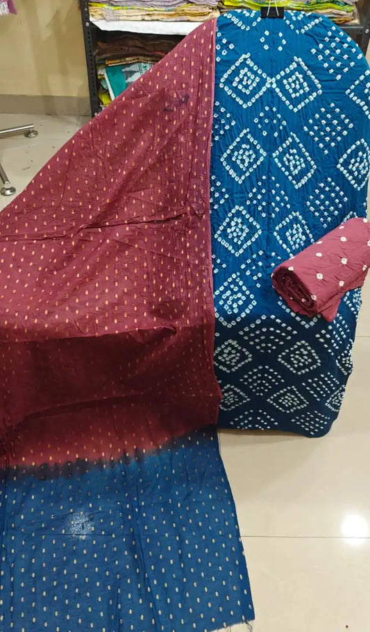 Vibrant teal blue unstitched cotton bandhani dress material with white diamond tie-dye patterns, paired with a contrast maroon dupatta featuring golden foil dots.