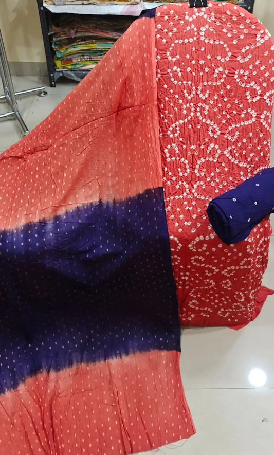 Vibrant coral orange unstitched bandhani suit fabric featuring rich geometric tie-dye patterns, styled with a deep royal blue contrast dupatta