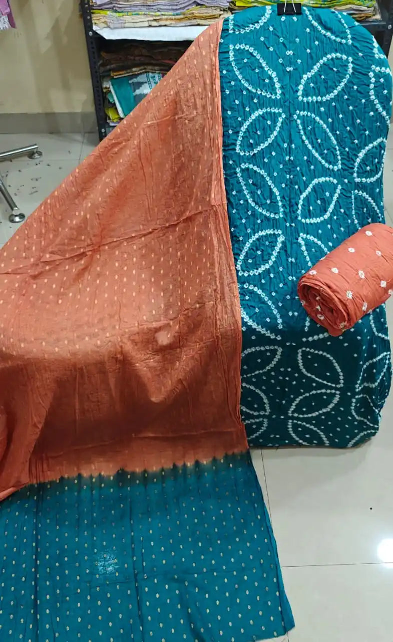Vibrant teal blue unstitched cotton bandhani dress material with geometric tie-dye layouts, styled with a warm rust-orange contrast dupatta.