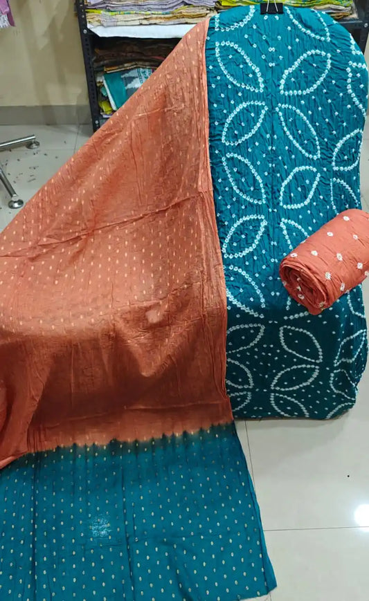 Vibrant teal blue unstitched cotton bandhani dress material with geometric tie-dye layouts, styled with a warm rust-orange contrast dupatta.