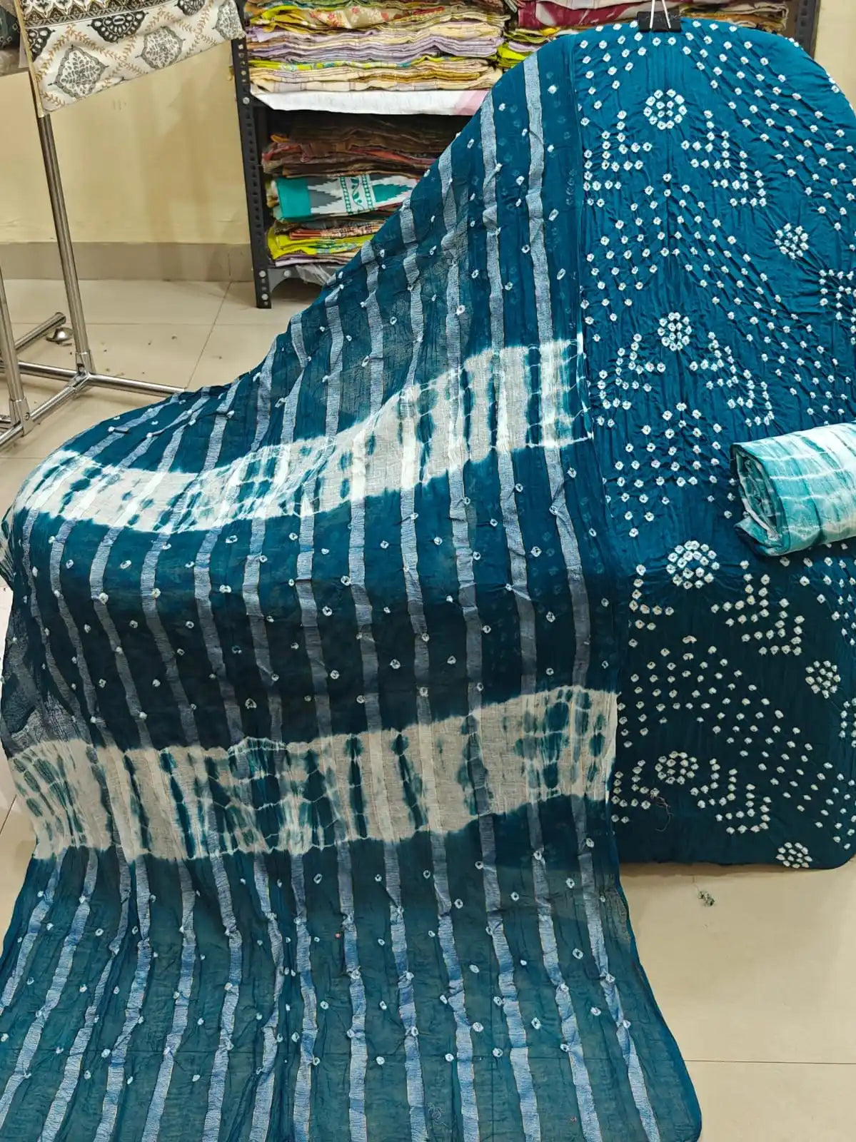 Vibrant teal blue unstitched cotton bandhani dress material with geometric tie-dye layouts, styled with a warm rust-orange contrast dupatta.