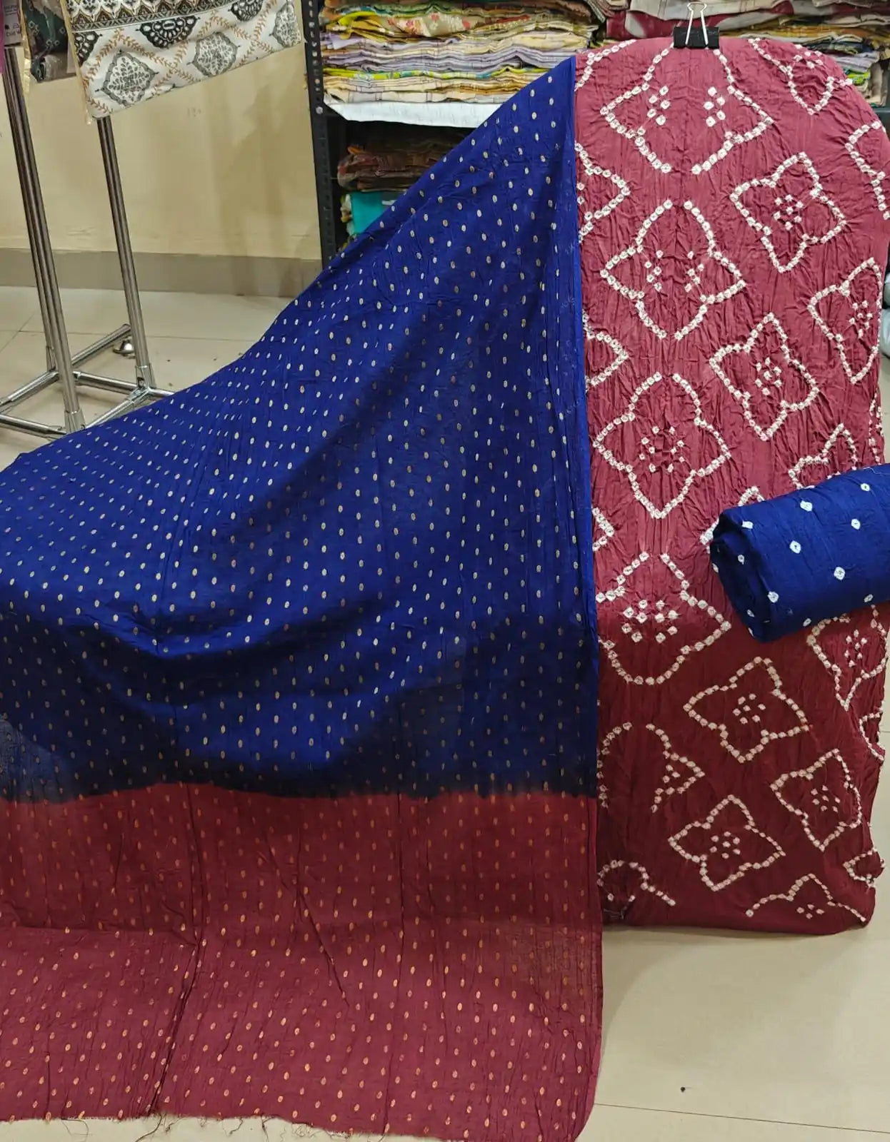 Rich maroon cotton bandhani dress material decorated with distinctive white diamond-shaped tie-dye patterns, paired with a vibrant royal blue dupatta showcasing gold accents and a matching blue bottom fabric.