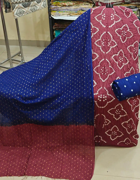 Rich maroon cotton bandhani dress material decorated with distinctive white diamond-shaped tie-dye patterns, paired with a vibrant royal blue dupatta showcasing gold accents and a matching blue bottom fabric.