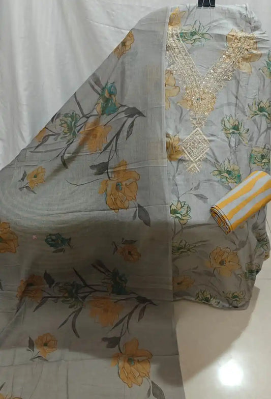 A stylish grey cotton unstitched suit fabric by ASC, featuring oversized golden-yellow flowers, an embroidered cream V-shape neck detail, and a coordinated printed dupatta.