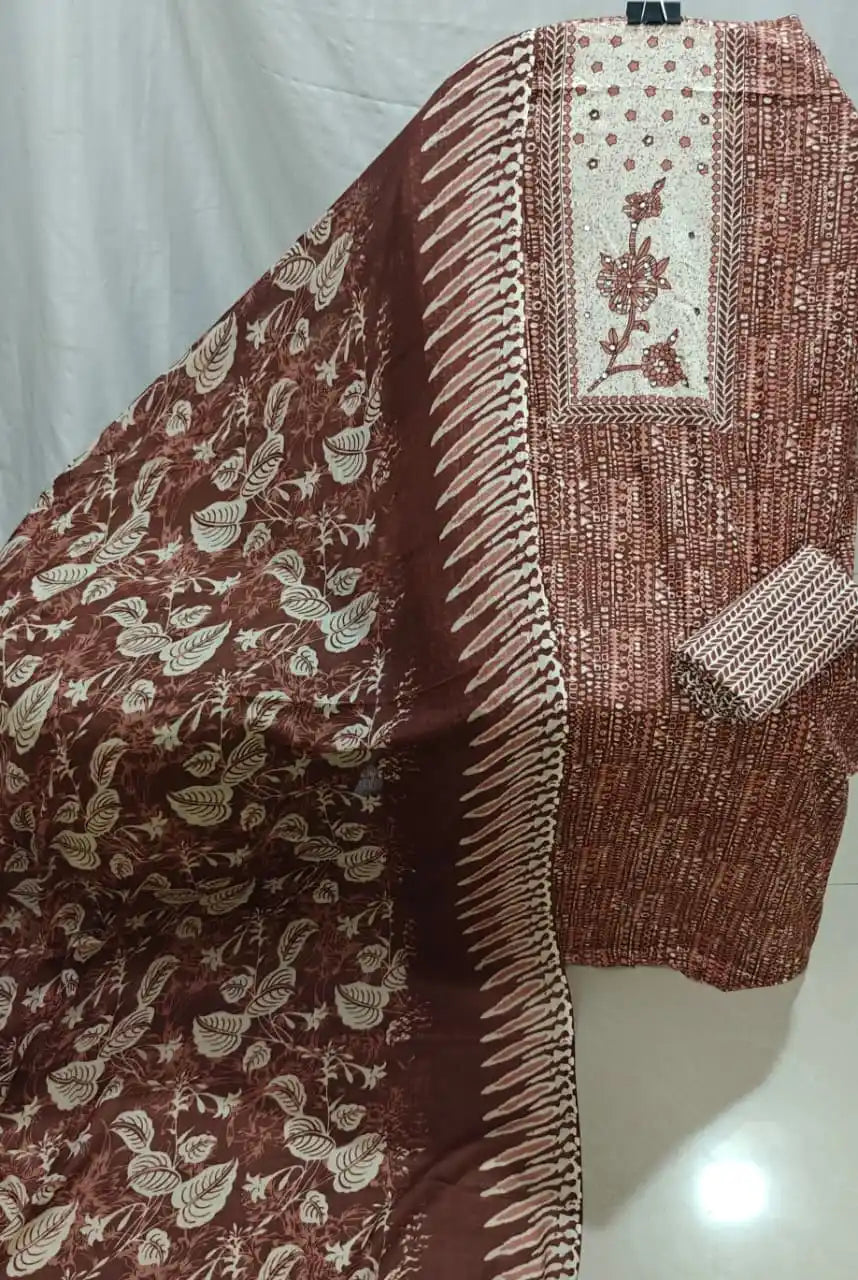 A detailed display of a rust-brown cotton unstitched dress material by ASC, featuring a fine textured geometric background pattern, an embroidered cream rectangular panel with elegant floral details, and a coordinated dark rust dupatta with white leaf motifs.