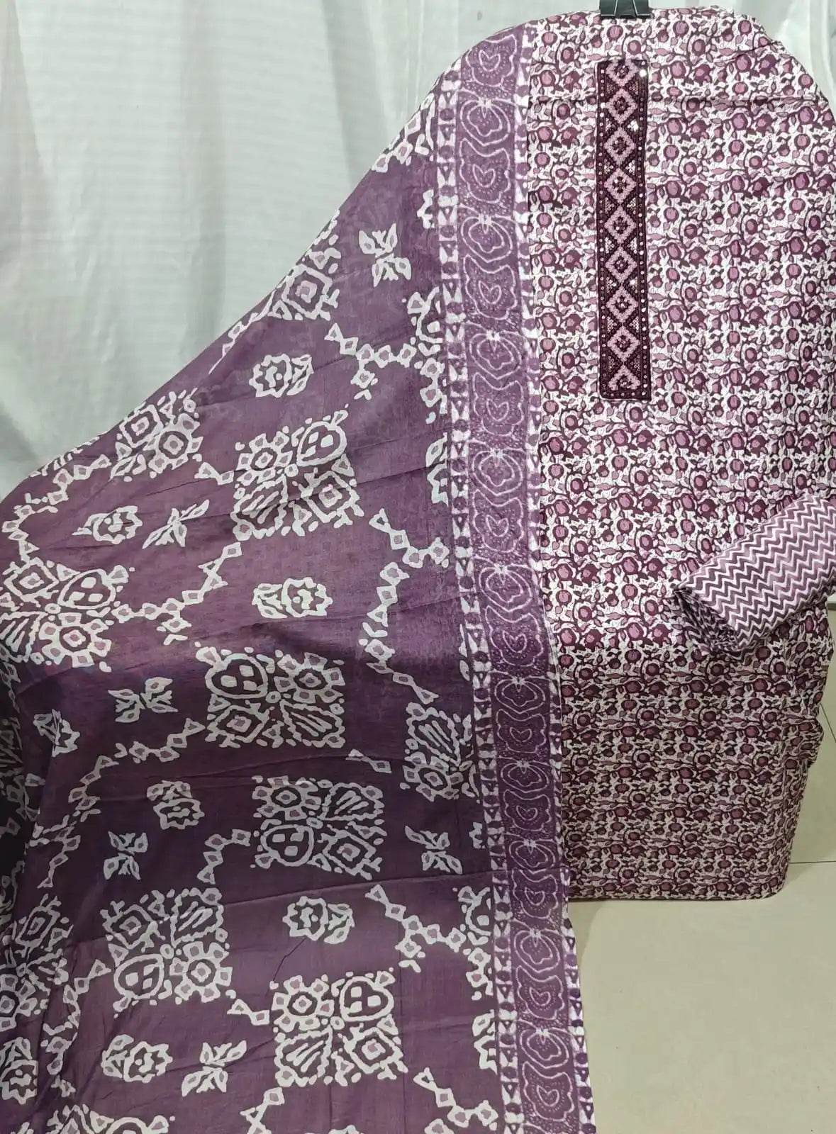 A neat presentation of a wine-toned cotton unstitched suit fabric by ASC, showcasing a fine floral jaal texture, a deep purple embroidered rectangular neck panel, and a coordinated wine dupatta with white geometric patterns.