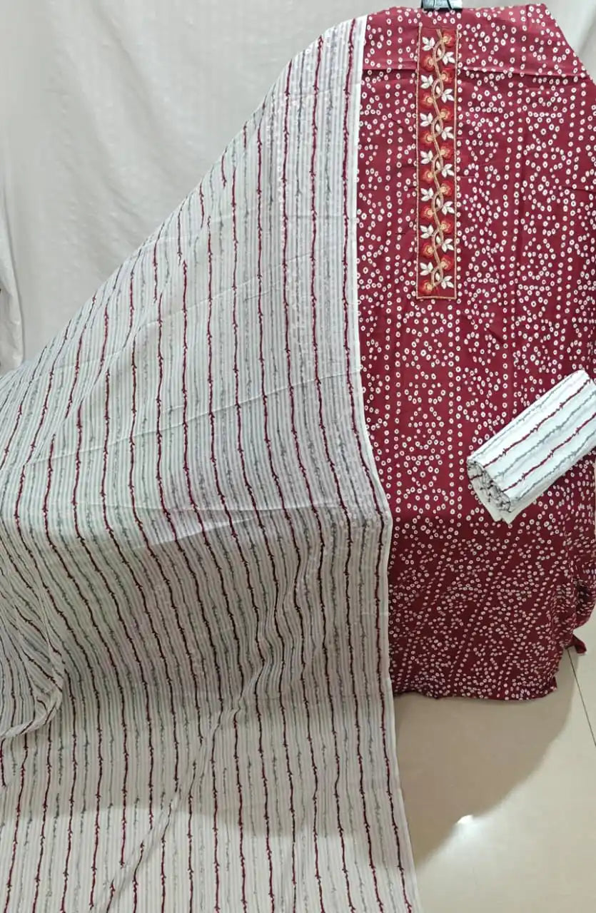 A rich deep maroon cotton unstitched dress material by ASC, featuring an all-over traditional micro white bandhani dot print on the shirt, a long vertical neck panel embroidered with golden leafy vines, a white bottom fabric with wavy maroon stripes, and a light-toned dupatta with vertical wavy striped patterns.