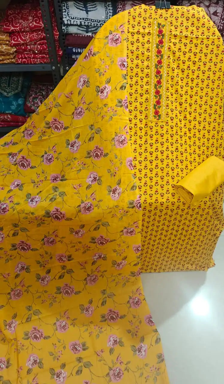 A vibrant sunny yellow cotton unstitched dress material by ASC, displaying small red-and-pink floral butis on the kurta, a red embroidered floral vine neck patch, a solid plain yellow bottom piece, and a matching yellow dupatta adorned with an all-over pink rose vine floral pattern.