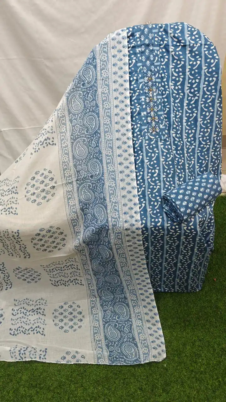 A beautiful slate blue and off-white cotton unstitched dress material by ASC, featuring a vertical batik-style dotted wave print on the shirt, a matching neck panel accented with handcrafted floral threadwork, a coordinated blue printed bottom fabric, and an off-white dupatta embellished with paisley motifs, traditional block borders, and circular block-print patches.