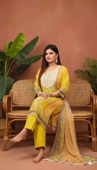 Pakistani designer suit with pearl embroidery worn by a woman sitting on a rattan chair with green plants.