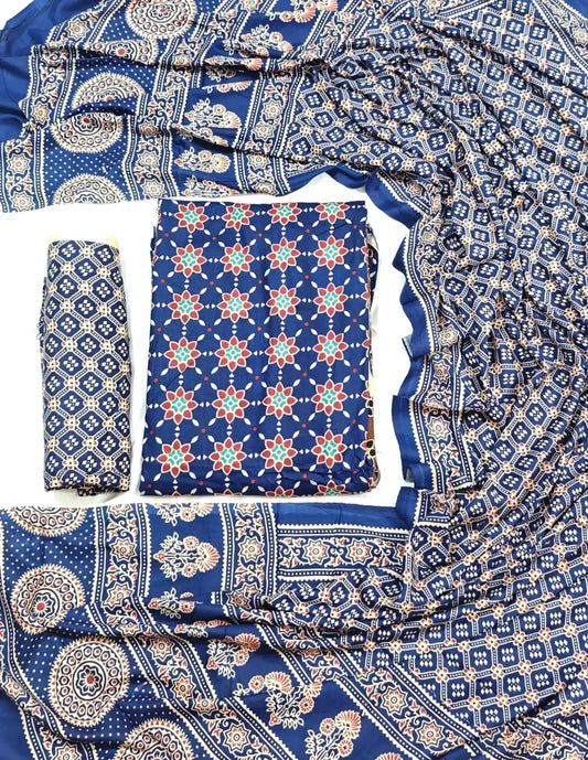 A vibrant royal blue rayon unstitched dress material by ASC, decorated with a red and teal floral star pattern on the shirt, a Kutchi geometric bottom piece, and a gracefully draped printed dupatta featuring intricate Ajrakh floral and circle borders.