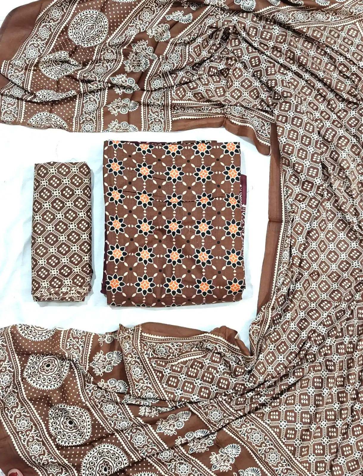 An elegant coffee brown rayon unstitched suit fabric by ASC, detailed with an orange and black star lattice design on the kurta, a Kutchi patterned bottom cloth, and an elaborate printed dupatta with traditional ethnic borders.
