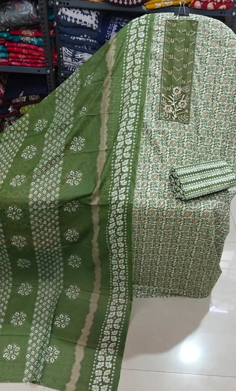 Olive green unstitched suit featuring floral block print artistry and detailed neck patch displayed on a shelf.