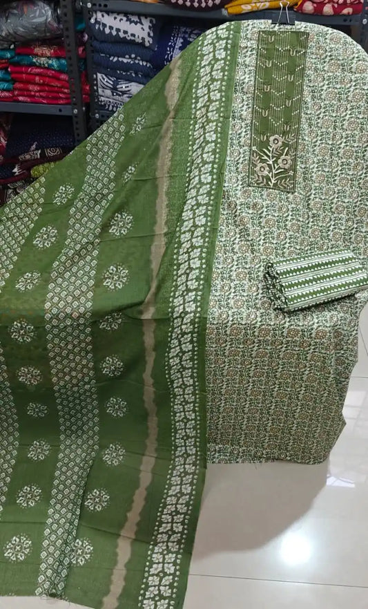 Olive green unstitched suit featuring floral block print artistry and detailed neck patch displayed on a shelf.