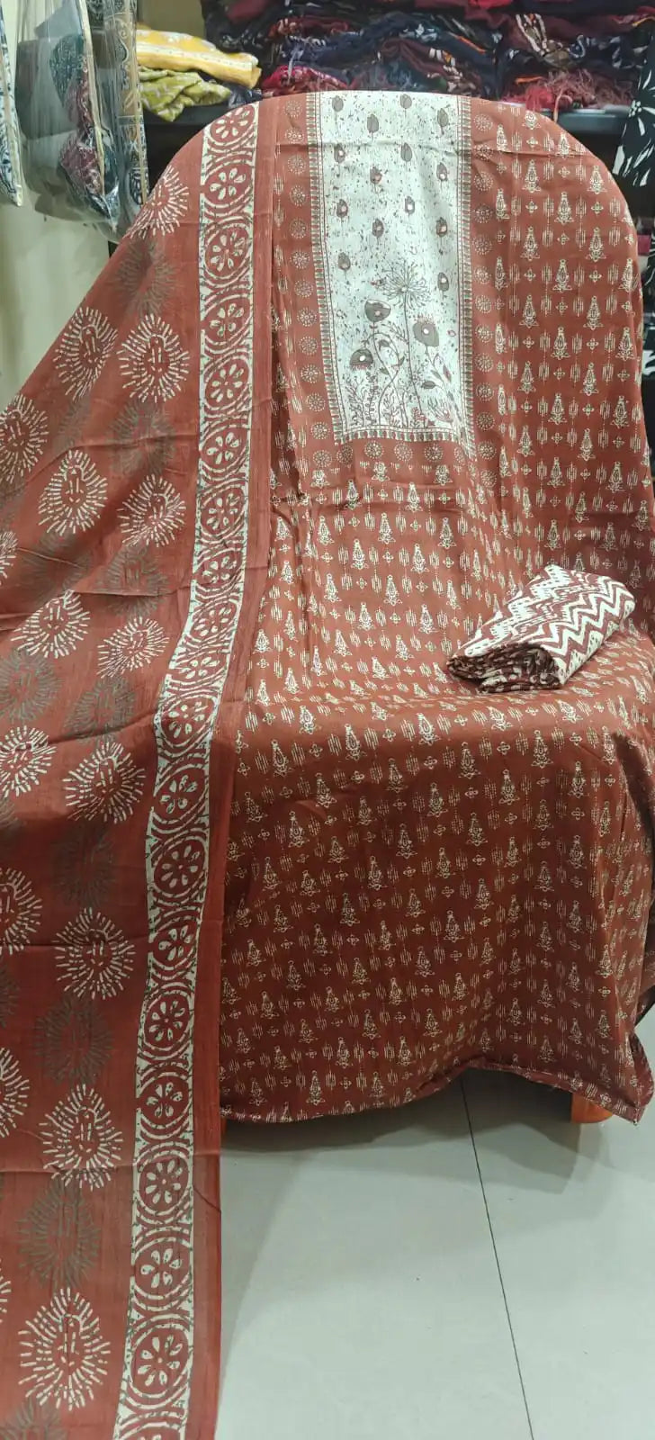 Rust orange cotton suit displaying a detailed white-and-grey embroidered neck panel, traditional wheel prints, and a matching bordered dupatta.