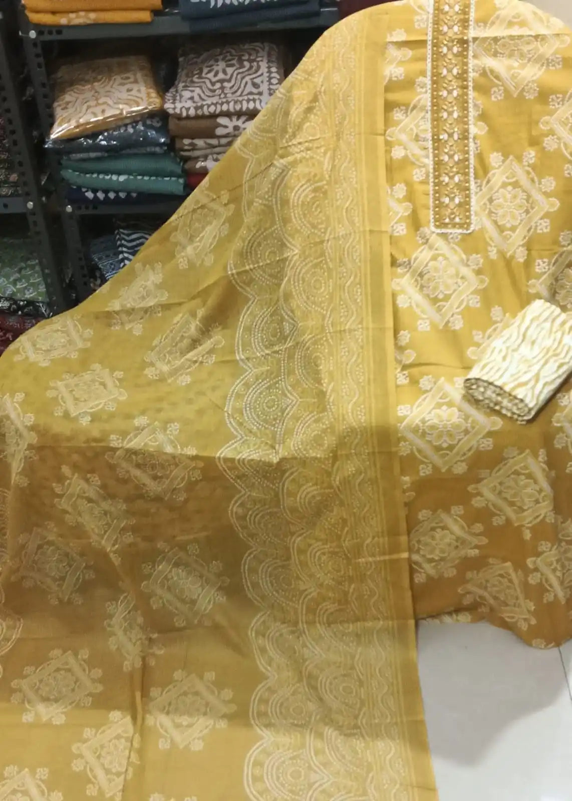 Bright mustard yellow cotton suit highlighting a heavily embroidered floral neck strip, traditional geometric Bandhani block prints, and a wavy-bordered matching dupatta.