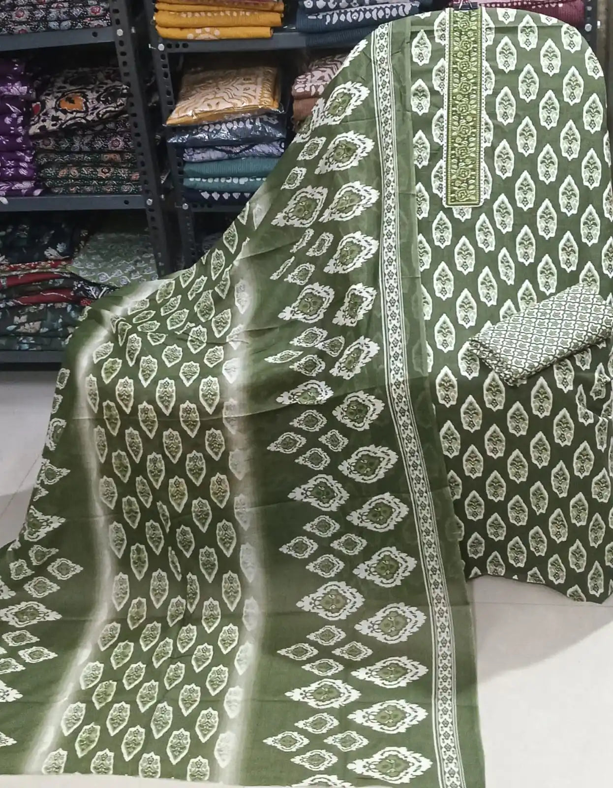 Deep olive green cotton suit showcasing a contrast green embroidered neck patch, traditional leaf-shaped ikat patterns, and a multi-shaded printed dupatta.