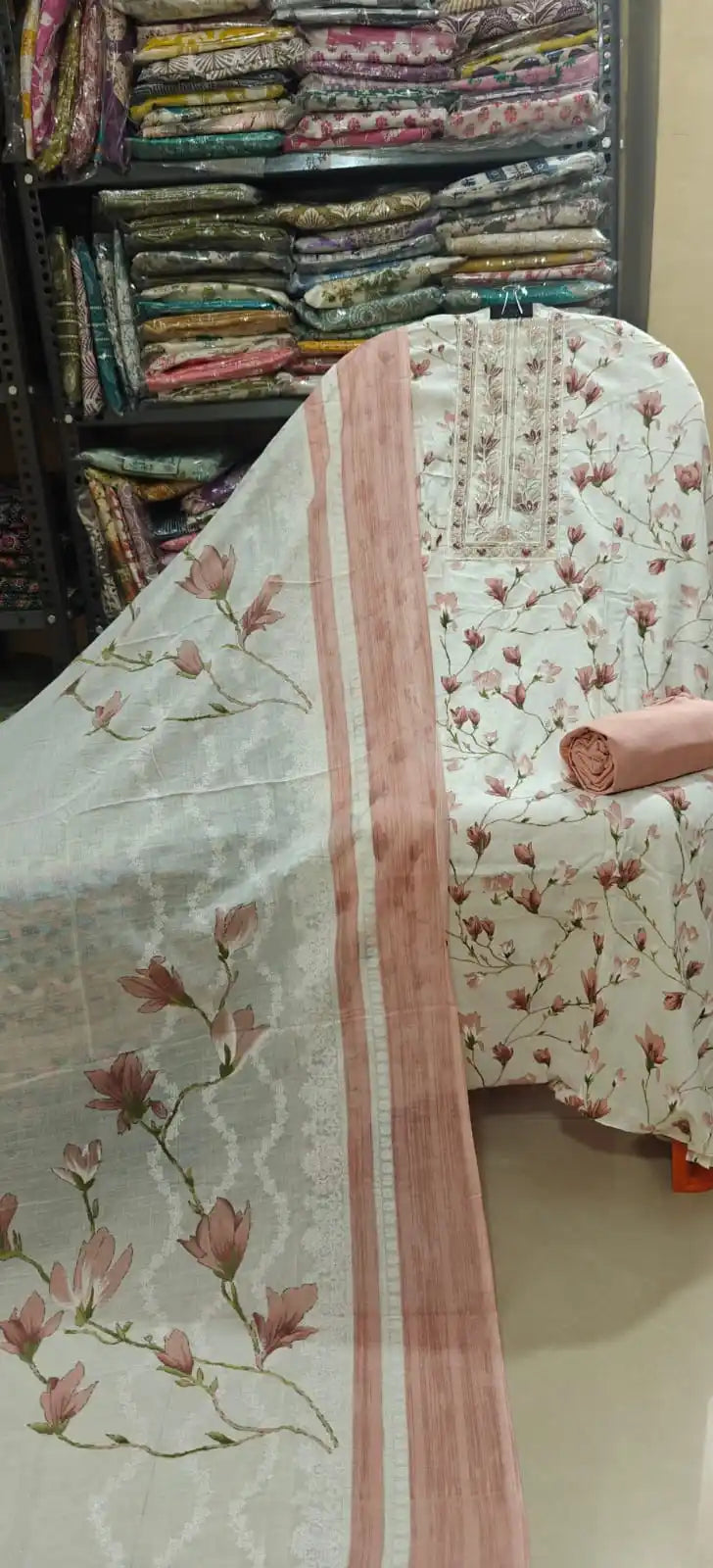 Off-white cotton suit material decorated with a beautiful pink magnolia floral print and an intricately embroidered neckline panel, paired with a solid dusty pink bottom and a matching bordered dupatta.