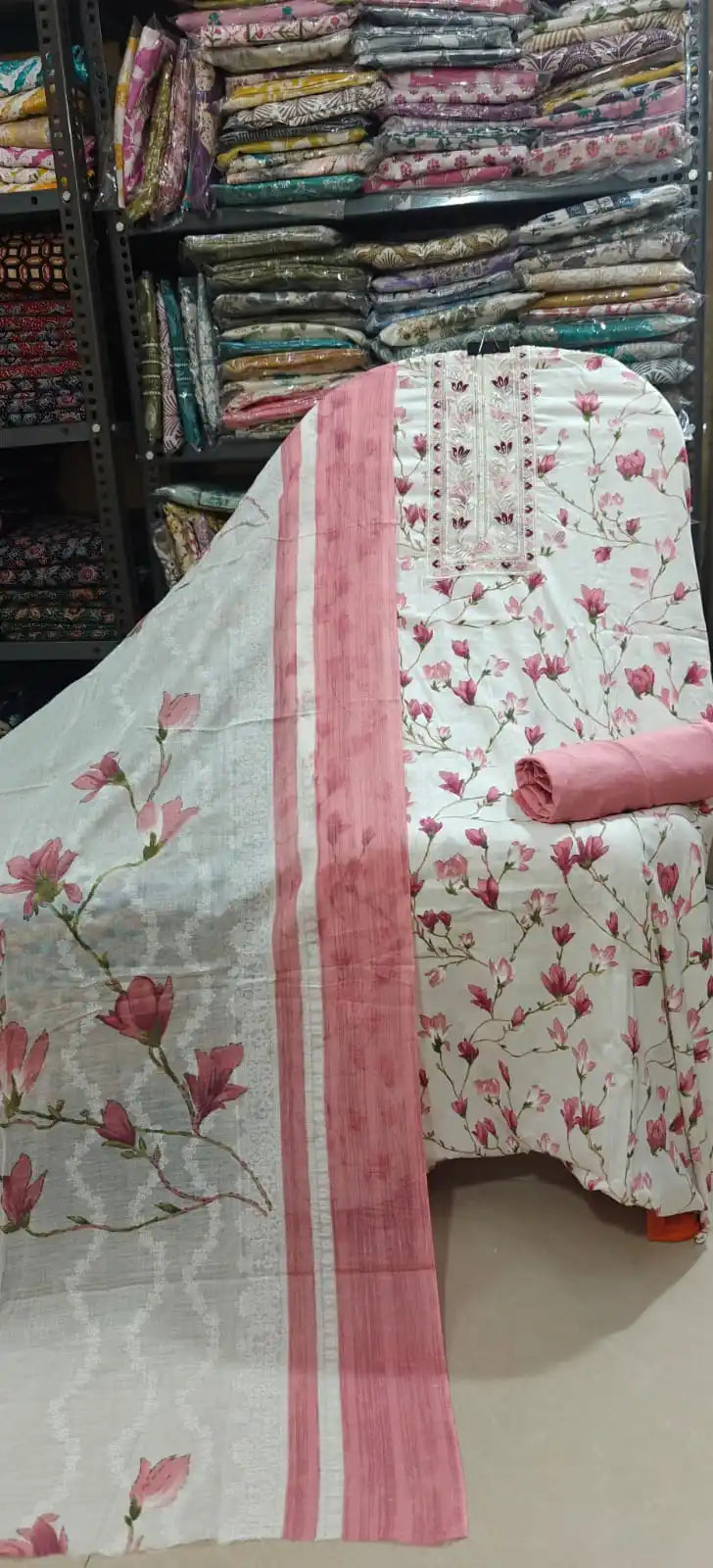 Clean white cotton suit fabric featuring a romantic pink floral vine print and a heavily detailed embroidered neck design, complete with a dusty rose bottom fabric and a coordinating dupatta.
