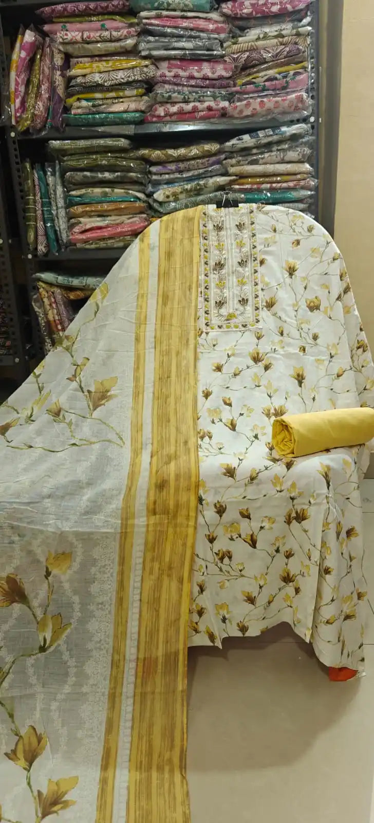 Light cream unstitched cotton dress material with a vibrant yellow-mustard floral print, a beautifully embroidered split neckline, a solid yellow bottom fabric, and a matching striped border dupatta.