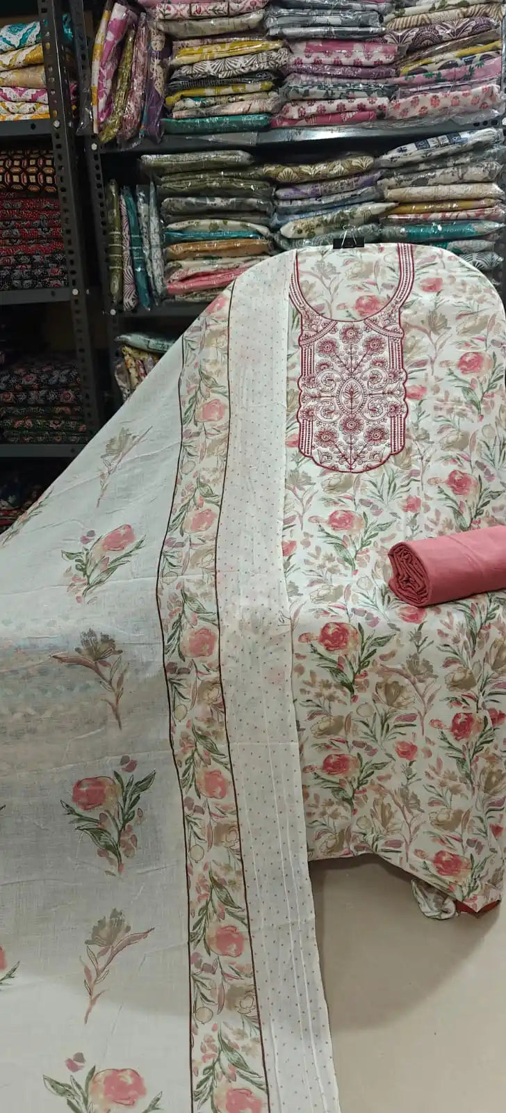 Light cream cotton suit fabric decorated with pink rose floral prints and an elaborate dark pink embroidered neckline, accompanied by a solid rose pink bottom fabric and a matching border dupatta.