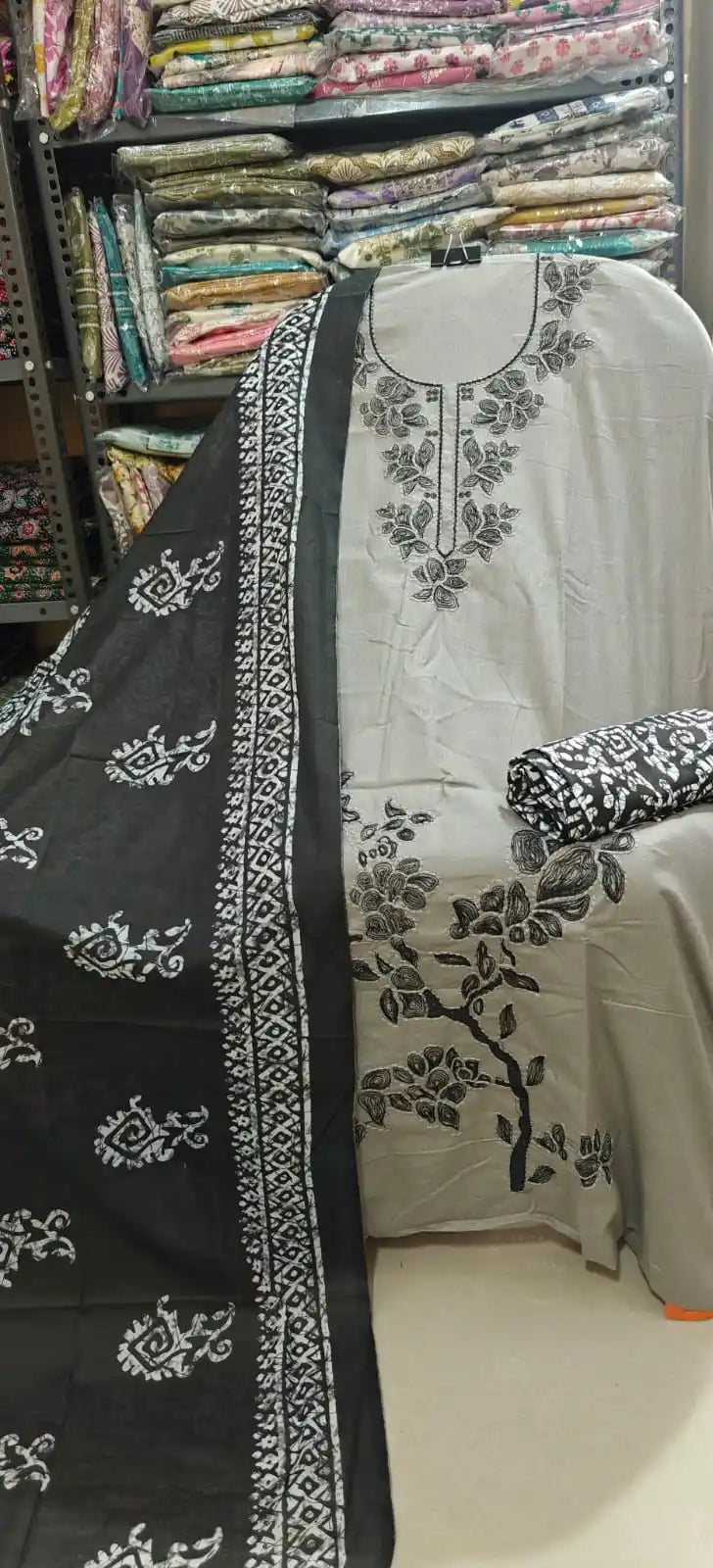 Minimalist grey-toned unstitched cotton suit featuring a bold black embroidered branch design on the side and neckline, paired with a contrasting black dupatta adorned with white block-print patterns and a matching printed bottom fabric.