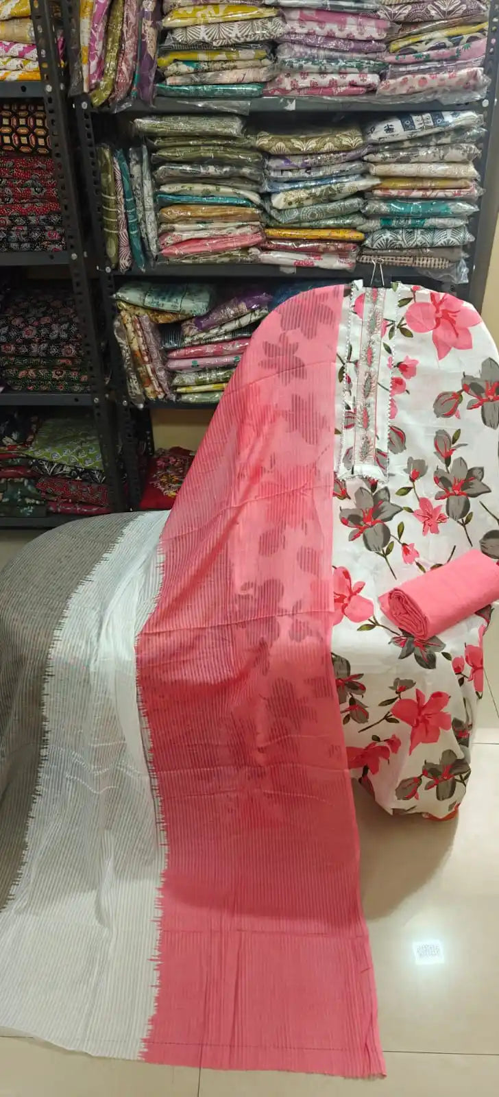 Crisp white unstitched cotton suit showcasing large bright pink and grey floral motifs, featuring a clean lace-trimmed neckline panel, paired with a solid pink bottom and a matching pink and grey striped dupatta.