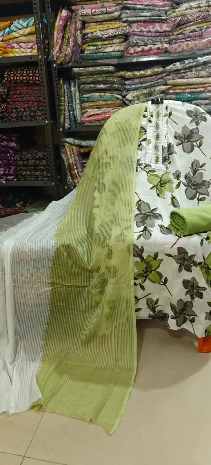 Clean white cotton salwar suit material decorated with olive-green and grey floral patterns, featuring a striped neck patch with lace borders, complete with a solid green bottom fabric and a matching green striped dupatta.