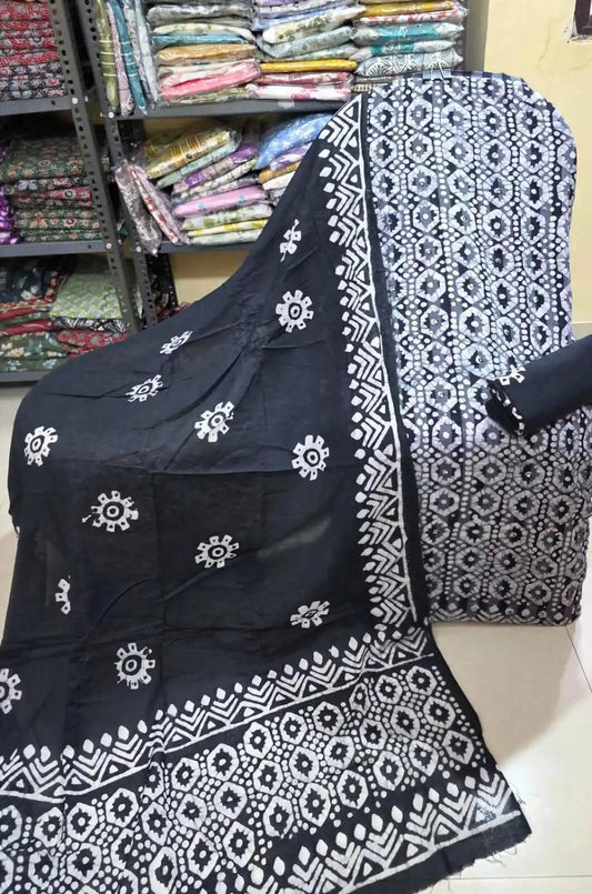 Classic black unstitched cotton salwar suit material displaying a contrasting white honeycomb batik design across the shirt panel, styled with a rolled black bottom fabric, and a matching black dupatta featuring white sunburst motifs and traditional batik borders.