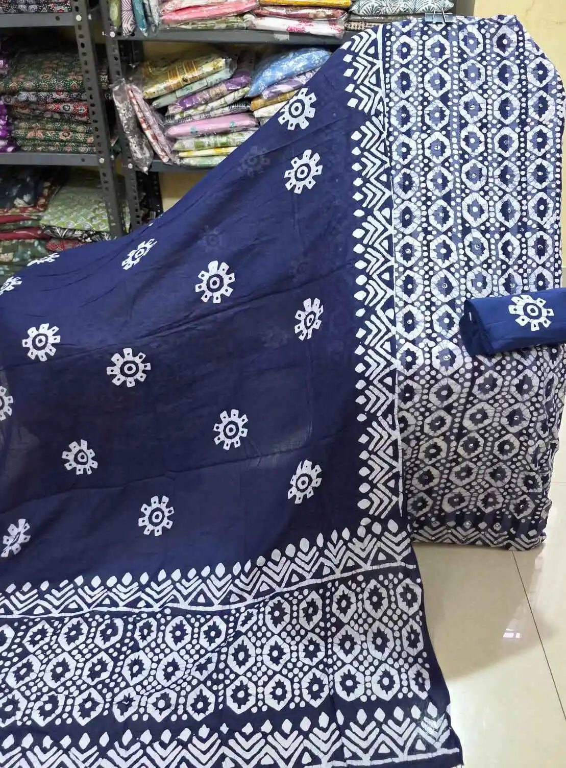 Deep navy blue cotton dress material featuring a structured white geometric batik pattern on the kameez fabric, paired with a solid navy blue bottom roll, and a matching navy blue dupatta accented with white floral-like batik stamps and wide borders.